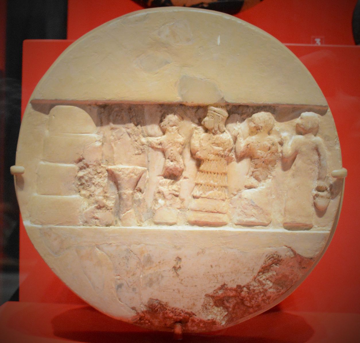 Disco de alabastro de Enheduanna, representada de frente para um suporte de planta durante um ritual. Atrás dela segue um padre e duas sacerdotisas. Unniversity of Philladelphia Museum.