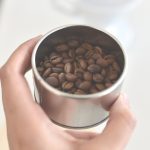 MÃO SEGURANDO COPO COM GRÃOS DE CAFÉ