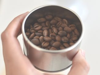 MÃO SEGURANDO COPO COM GRÃOS DE CAFÉ