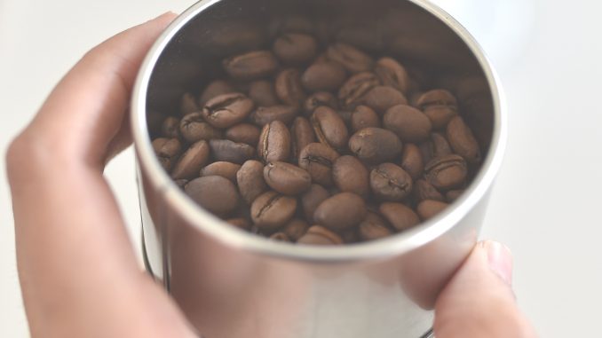 MÃO SEGURANDO COPO COM GRÃOS DE CAFÉ
