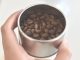 MÃO SEGURANDO COPO COM GRÃOS DE CAFÉ