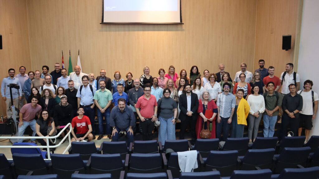 Foto de diversas pessoas reunidas lado a lado, a maioria em pé e algumas agachadas. Todas as pessoas olham para a foto.