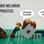 Conjunto de peças lego onde dois bonecos estão empurrando um carrinho sem rodas ao lado e outro está segurando duas rodas. O diálogo sugere que as rodas melhorariam o trabalho.