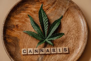 folha verde de sete pontas, sobre um prato de madeira e, abaixo da folha, há quadrados de madeira com letras combinadas formando a palavra Cannabis.