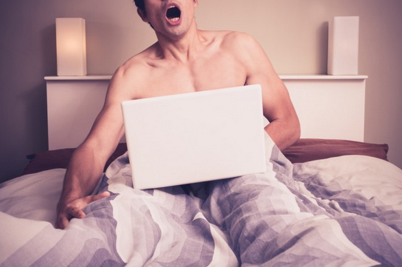 Imagem: Young man is sitting in bed and watching pornography on laptop. LoloStock/Shutterstock